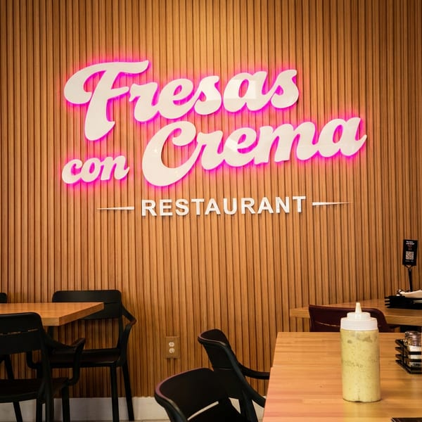 The Fresas con Crema restaurant interior features a neon sign, wooden slat wall, and empty tables.