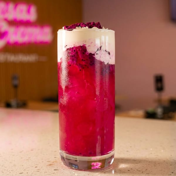 Vibrant pink dragon fruit drink with white foam and fruit chunks on a counter at Fresas & Crema.